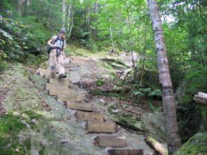 A Dartmouth Outing Club trail crew worker descends wooden steps pinned to a steep ledge on Mount Moosilauke’s Beaver Brook Trail