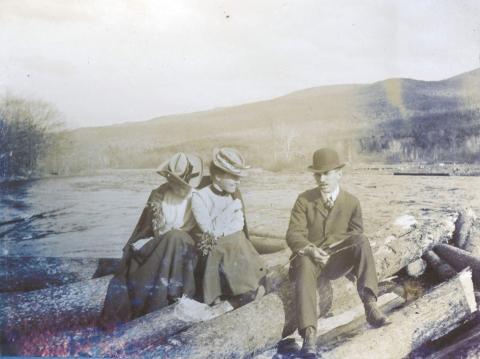 Two women and a man sitting on jam logs near Fuller Farm