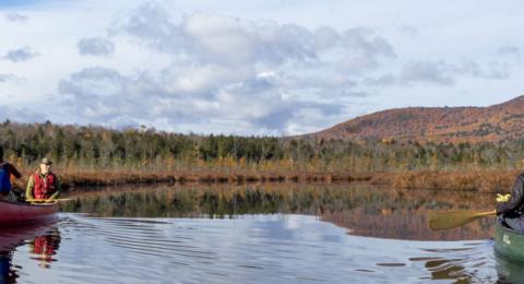 Students are canoeing on two separate canoes on a large lake overseeing the mountains