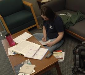 Student sitting cross-legged on the floor surrounded by notebooks and papers