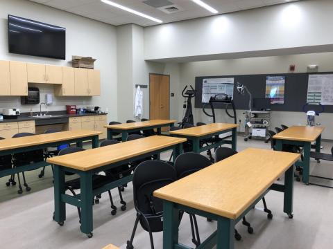 A classroom with 5 long tables with 2 chairs each with laboratory stations in the back of the room.