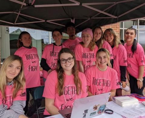 Students sit and stand under a tent at an event hosted by Campus Recreation to raise awareness about and fight Breast Cancer.
