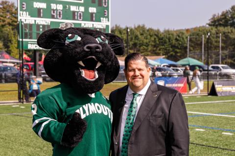 Photo of PSU panther mascot standing on a sports field with a man, Todd Angilly, in a suit and tie