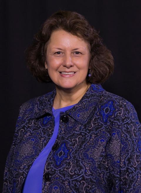 Professional headshot of a woman smiling and wearing a purple paisley suit.