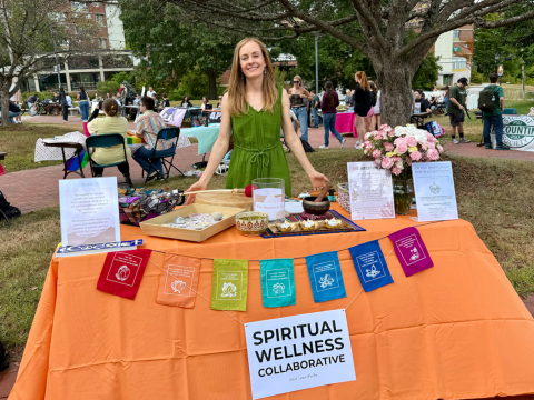 Woman smiling in back of a display table reading "Spiritual Wellness Collaborative"
