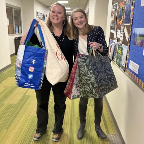 Two females holding gift bags, smiling.