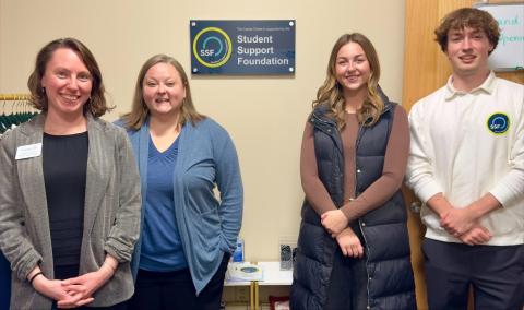 Two women stand on opposite ends of another woman and a man, all members of the Student Support Foundation; the logo is shown on the wall behind them.