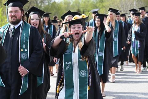 A group of graduates are walking together, one student points at the camera with a happy expression.