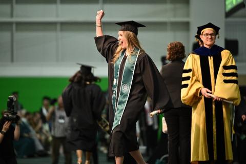 Graduate is seen getting her photo taken. She raises her fist up with a happy expression on her face.
