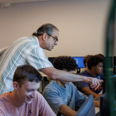 Professor is seen pointing at a computer screen, assisting a student.