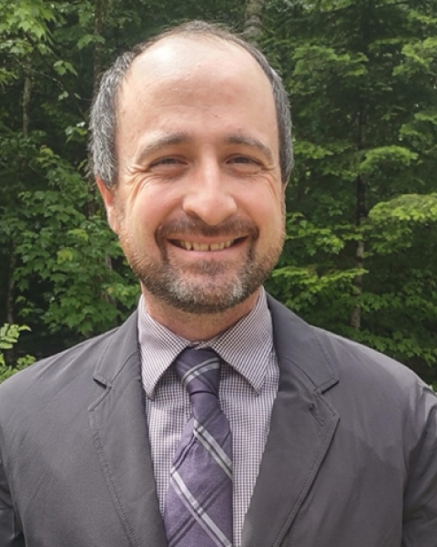 A man is seen smiling. He wears a business suit.